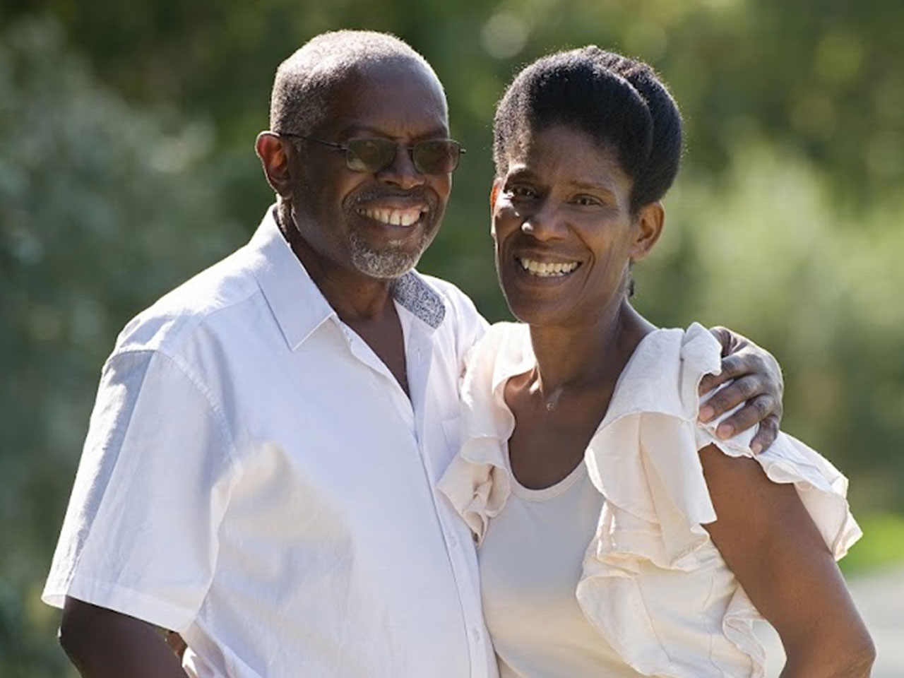 Husband and wife stand in a green field both wearing white