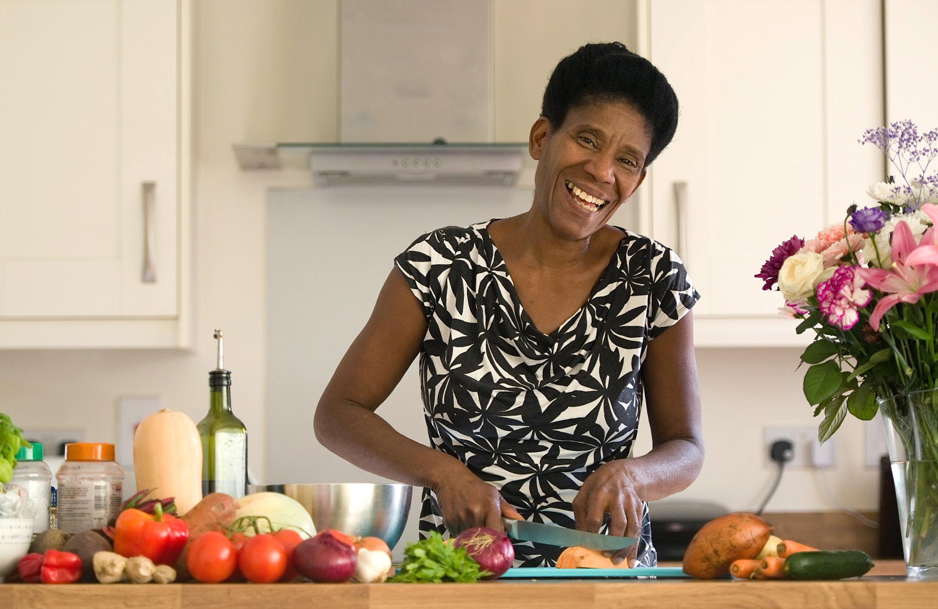 Rowena cuts vegetables in the kitchen while smiling at the camera