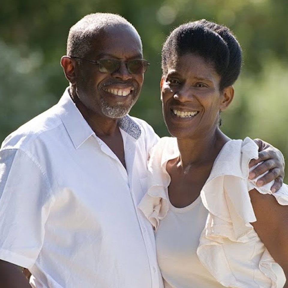 Sam-and-Rowena-edit Husband and wife stand in a green field both wearing white